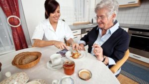 a geriatric nurse helps elderly woman at breakfast